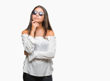 Genç güzel Arap kadın elle çene düşünme hakkında soru, dalgın ifade izole arka plan üzerinde güneş gözlüğü takıyor. Düşünceli yüzüyle gülümsüyor. Şüphe kavramı.