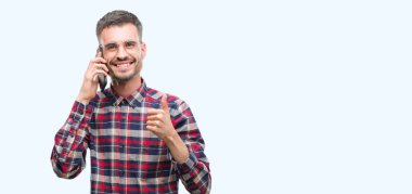 Telefonda büyük mutlu ile konuşan genç yenilikçi yetişkin adam gülümseme ok işareti, başparmak ile parmak, mükemmel işareti yapıyor