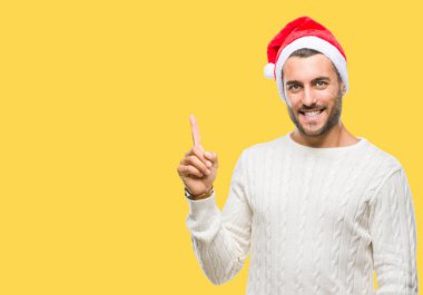 Kameraya bakarak yan el ve parmak ile işaret yüzünde kocaman bir gülümseme ile izole arka plan üzerinde santa claus şapka giyen genç yakışıklı adam.