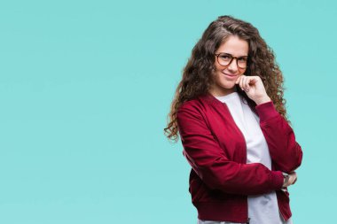 Güzel esmer kıvırcık saçlı Genç kız emin çapraz kollar ve çeneme kaldırdı el ile gülümseme ile kameraya bakarak izole arka plan üzerinde ceket ve gözlük takıyor. Pozitif düşünce.