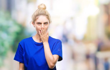 İzole arka plan üzerinde mavi t-shirt giyen genç güzel sarışın ve mavi gözlü kadın esneme yorgun kapsayan ağız el ile sıkılmış. Restless ve uyku hali.