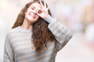 Gülümseyen, parmakları ile mutlu yüz üzerinden seyir göz el ile ok jest yapıyor izole arka plan üzerinde kış kazak giyen güzel esmer kıvırcık saçlı Genç kız.