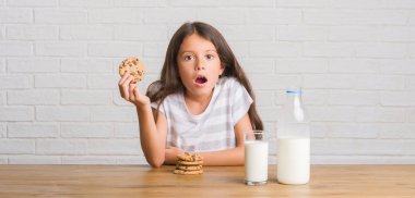 Süt içme ve çikolata bisküvi bir sürpriz yüz, korkuyor ve heyecanlı korku ifadesi ile şok korkmuş yemek masada oturan genç İspanyol çocuk