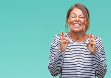 Orta yaş İspanyol kadın kıdemli geçiş parmakları umut ve gözleri kapalı ile gülümseyen izole arka plan üzerinde. Şans ve batıl kavramı.