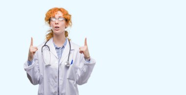 Doktor üniforması giyen genç Kızıl saçlı kadın hayrete ve yukarıya bakıyor ve parmakları ile işaret ve silah kaldırdı şaşırttı.