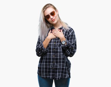 Genç Sarışın kadın ile gülümseyen izole arka plan üzerinde güneş gözlüğü takıyor kapalı gözler ve yüzünde minnettar jest ile göğüs üzerinde eller. Sağlık kavramı.