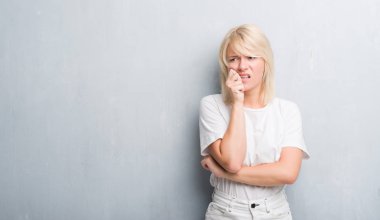 Grunge gri duvar stresli ve gergin elle çivi ısırma ağzına seyir yetişkin beyaz kadın. Anksiyete sorunu.