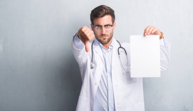 Yakışıklı genç doktor adam gri grunge duvar sayfa boş sözleşme kızgın yüzü, eksi işareti aşağı antipati başparmak ile gösterilen, ret kavramı ile tutarak
