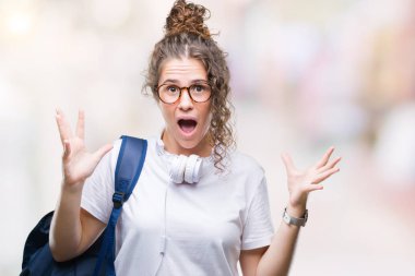 Sırt çantası ve kulaklık üzerinde giyen genç esmer öğrenci kız arka plan deli kutluyor izole ve crazy arms ile başarı için kaldırdı ve heyecanlı çığlık gözler kapalı. Kazanan kavramı