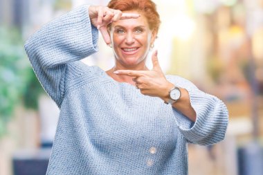 Elle yapma çerçeve ve parmakları ile mutlu yüz gülümseyen izole arka plan üzerinde kış kazak giyen Atrractive üst düzey beyaz Kızıl saçlı kadın. Yaratıcılık ve Fotoğrafçılık kavramı.