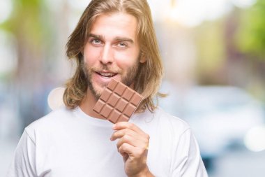Uzun saç beslenme ile yakışıklı delikanlı çikolata bar acımak yüz ciddi düşünüyorum üstünde kendine güvenen bir ifade ile izole arka plan üzerinde