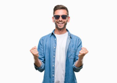 Yakışıklı delikanlı izole arka plan kutlama üzerinde güneş gözlüğü takıyor şaşırttı ve başarı için kaldırdı kollarını açarak hayret ve gözleri açık. Kazanan kavramı.