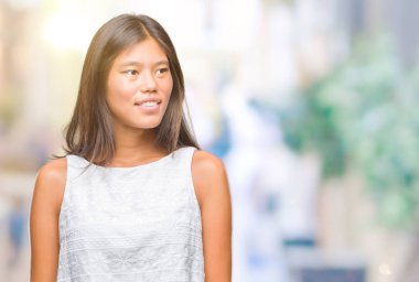 Genç Asyalı kadın uzak tarafına yüzünde, doğal ifade gülümseme ile seyir izole arka plan üzerinde. Kendine güvenen gülüyor.