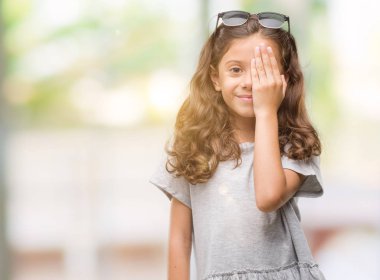 Esmer Latin kız yüz ve sürpriz duygu kendinden emin gülümseme ile el ile bir göz kapsayan güneş gözlüğü takıyor.