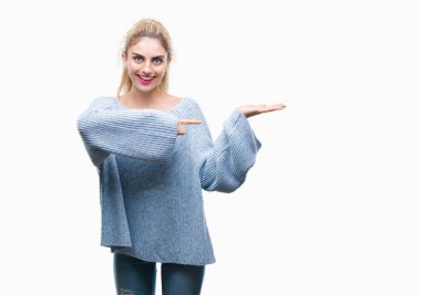 Hayret ve el ile sunulması ve parmak ile işaret ederken kameraya gülümseyen izole arka plan üzerinde kış kazak giyen genç güzel sarışın ve mavi gözlü kadın.