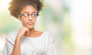 Genç afro Amerikalı kadın gözlük ile izole arka plan üzerinde çene düşünme hakkında soru, dalgın ifade ver. Düşünceli yüzüyle gülümsüyor. Şüphe kavramı.