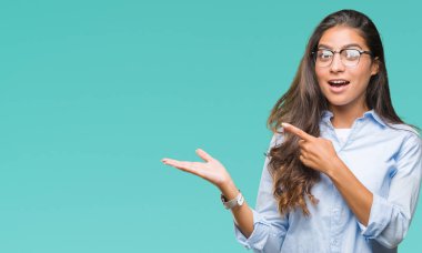 Genç güzel Arap kadın hayrete ve el ile sunulması ve parmak ile işaret ederken kameraya gülümseyen izole arka plan üzerinde gözlük.