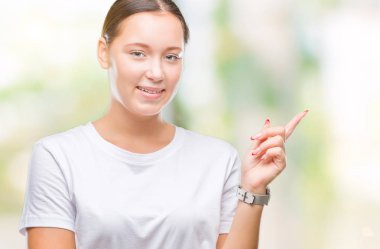 Yüzünde kocaman bir gülümseme ile izole arka plan üzerinde genç güzel beyaz kadın kameraya bakarak yan el ve parmak ile işaret.