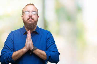 Ellerle birlikte AF emin gülümseyen için soran dua izole arka plan üzerinde gözlük takan Genç beyaz hipster adam.