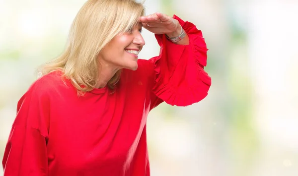 Middle age blonde woman over isolated background very happy and smiling looking far away with hand over head. Searching concept.