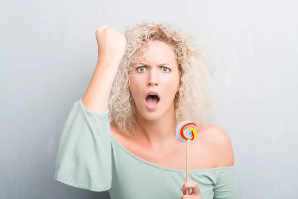 Joven Mujer Rubia Sobre Grunge Gris Pared Comer Caramelo Piruleta — Foto de Stock