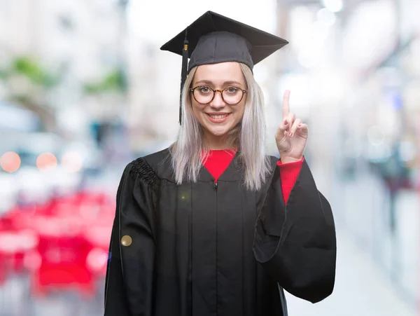 年轻的金发碧眼的女人穿着毕业制服在孤立的背景指向手指与成功的想法 离开和快乐 — 图库照片