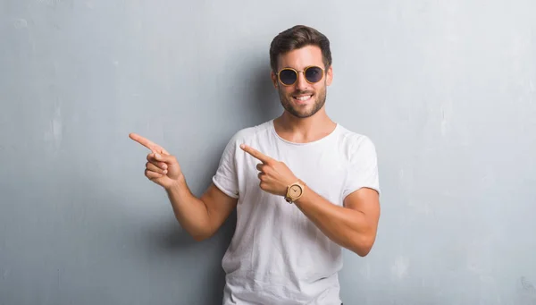 Joven Guapo Sobre Una Pared Grunge Gris Con Gafas Sol —  Fotos de Stock