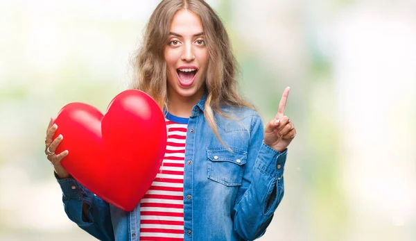 Linda Jovem Loira Segurando Coração Valentine Sobre Fundo Isolado Surpreso — Fotografia de Stock