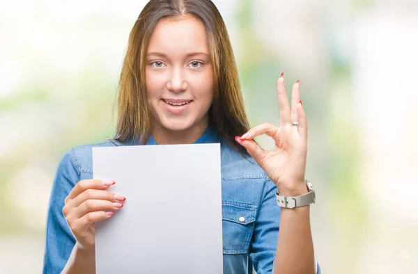 優秀なシンボルの指で サインをして孤立した背景に空白の紙のシートを保持している若い白人女性 — ストック写真