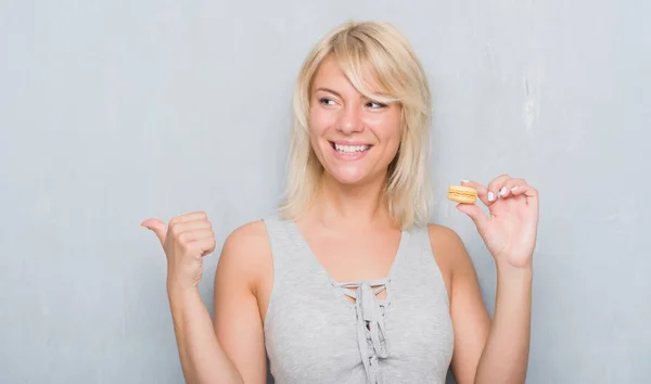 Mujer Caucásica Adulta Sobre Pared Gris Grunge Comiendo Macaron Señalando —  Fotos de Stock