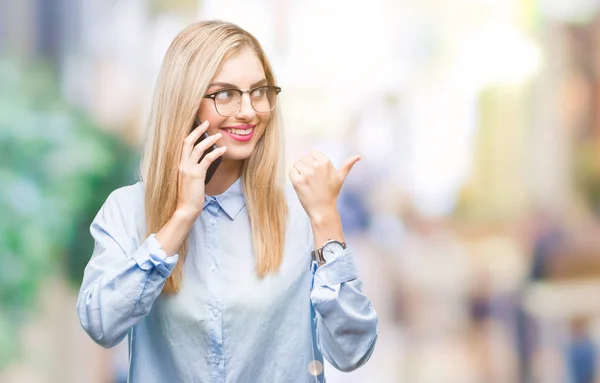 年轻美丽的金发女商人呼吁智能手机在孤立的背景指向和显示与幸福的脸微笑着的拇指和侧面 — 图库照片
