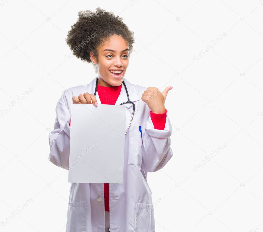 Young afro american doctor woman holding blank paper over isolated background pointing and showing with thumb up to the side with happy face smiling