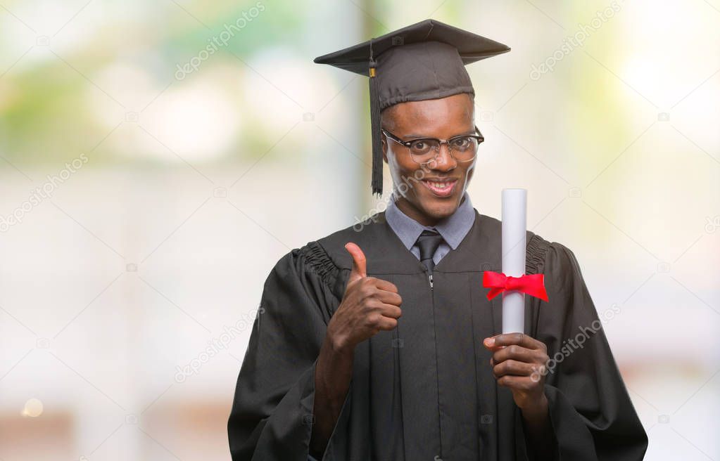 Young graduated african american man holding degree over isolated background happy with big smile doing ok sign, thumb up with fingers, excellent sign