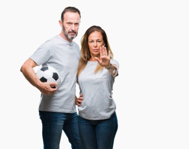 Orta yaş İspanyol çift ile izole arka plan üzerinde futbol futbol topu tutan el dur işareti ile ciddi ve kendine güvenen ifade, savunma jest yapıyor açın