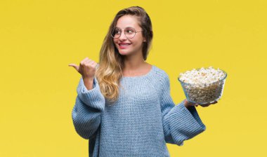 Genç güzel sarışın kadın işaret ve başparmak kadar mutlu yüz gülümseyen tarafı ile gösteren izole arka plan üzerinde patlamış mısır yemek