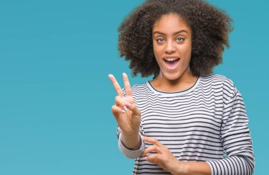 Mutlu yüz zafer işareti yaparken kameraya göz kırpıyor ile gülümseyen izole arka plan üzerinde genç afro Amerikalı kadın. İki numaralı.
