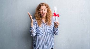 Genç redhead iş kadını ile çığlık zaferini kutluyor diploması çok mutlu ve heyecanlı, kazanan ifade büyük holding gri grunge duvarın üzerinden gülümse ve el kaldırdı