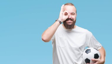 Mutlu yüz el parmaklarının arasından seyir göz üzerinde ok işaretiyle yapıyor gülümseyen izole arka plan üzerinde futbol futbol topu tutan genç beyaz hipster adam