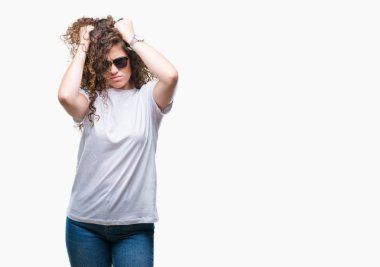 Güzel esmer kıvırcık saçlı Genç kız çünkü umutsuz ve stresli baş ağrısı acı izole arka plan üzerinde güneş gözlüğü takıyor ağrı ve migren. Ellerini kafasına.