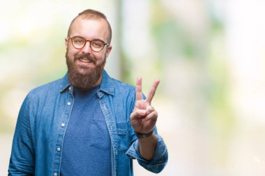 Mutlu yüz zafer işareti yaparken kameraya göz kırpıyor ile gülümseyen izole arka plan üzerinde gözlük takan Genç beyaz hipster adam. İki numaralı.