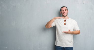 Beyaz delikanlı üzerinde gri grunge duvar eller eller büyük gösterilen ve büyük boy işareti, ölçü birimi sembolü ile güneş gözlüğü takıyor. Kameraya bakarak gülümsüyordu. Ölçüm kavramı.