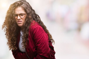 Güzel esmer kıvırcık saçlı Genç kız üzerinde ceket ve gözlük takıyor izole mide üzerinde el ile arka plan çünkü mide bulantısı, ağrılı hastalık hasta hissediyor. Ağrısı kavramı.