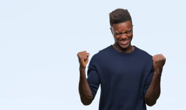 Gülümseyen ve başarı için çığlık genç Afro-Amerikan adam izole arka plan çok mutlu ve heyecanlı kaldırdı, silah ile kazanan jest yapıyor. Kutlama kavramı.