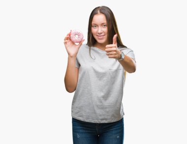 Ok işareti, başparmak ile parmak, mükemmel işareti yapıyor kocaman bir gülümseme ile izole arka plan üzerinde mutlu tatlı çörek yiyen genç kafkas kadın