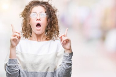 Güzel esmer kıvırcık saçlı Genç kız izole arka plan üzerinde gözlük hayret ve yukarıya bakıp parmakları ile işaret şaşırttı ve silah kaldırdı.