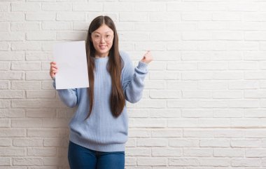 Duygu tezahürat Genç Çinli kadın gurur çığlık ve zafer ve başarı çok heyecanlı, kutluyor boş kağıt tutan tuğla duvarın üzerinden