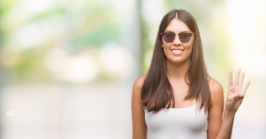 Dört kendinden emin ve mutlu gülümseyerek sırasında gösterilen ve parmakları ile işaret genç güzel İspanyol giyen güneş gözlüğü numara.