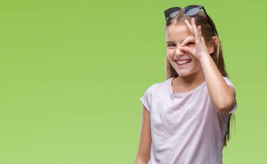 Genç güzel kız gülümsüyor, parmakları ile mutlu yüz üzerinden seyir göz el ile ok jest yapıyor izole arka plan üzerinde güneş gözlüğü takıyor.