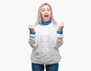 İzole arka plan üzerinde kutluyor kış kazak giyen genç sarışın kadın şaşırttı ve başarı için kaldırdı kollarını açarak hayret ve gözleri açık. Kazanan kavramı.