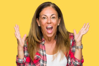 Orta yaş yetişkin kadın üzerinde rahat gömlek giymiş deli kutluyor arka plan izole ve başarı için kaldırdı kollarını açarak hayrete ve heyecanlı çığlık gözleri açık. Kazanan kavramı